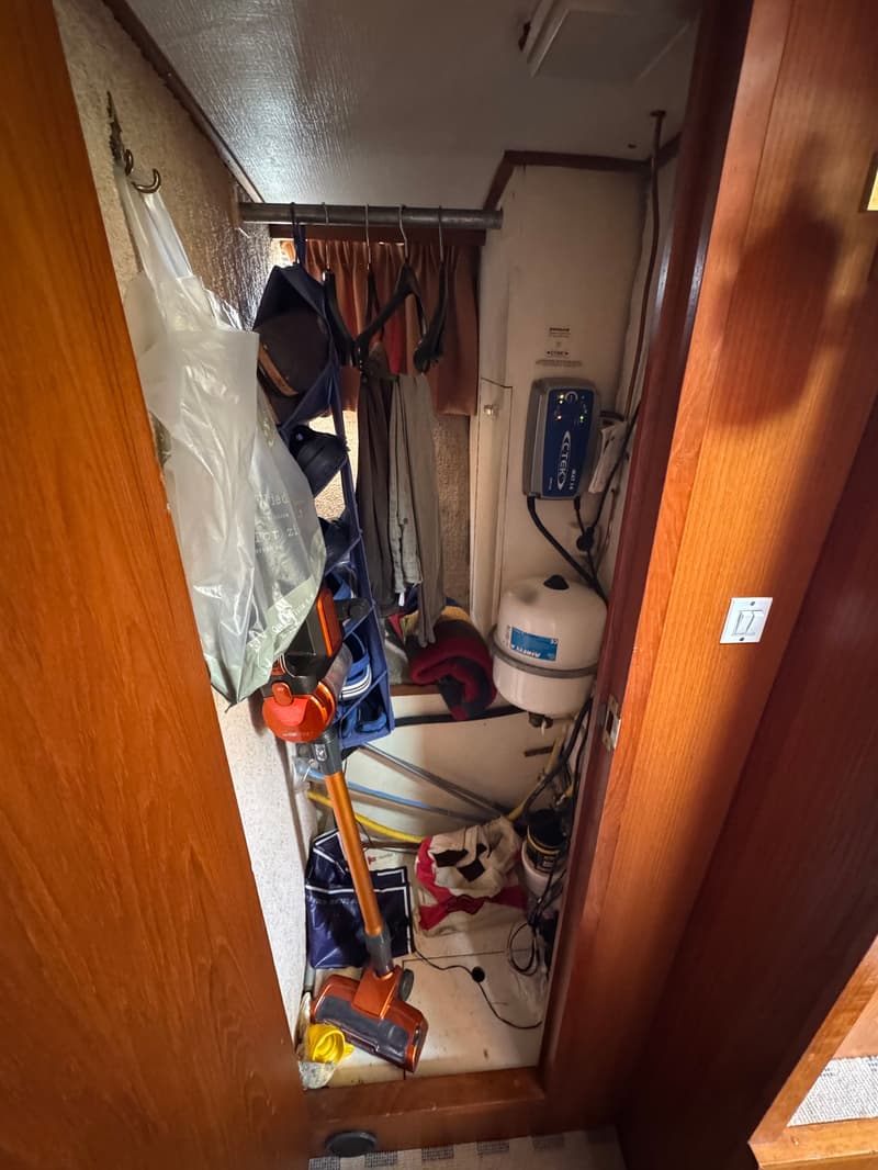 Een rommelige opbergruimte met een stofzuiger, tassen, kleding, een acculader en een drukvat.