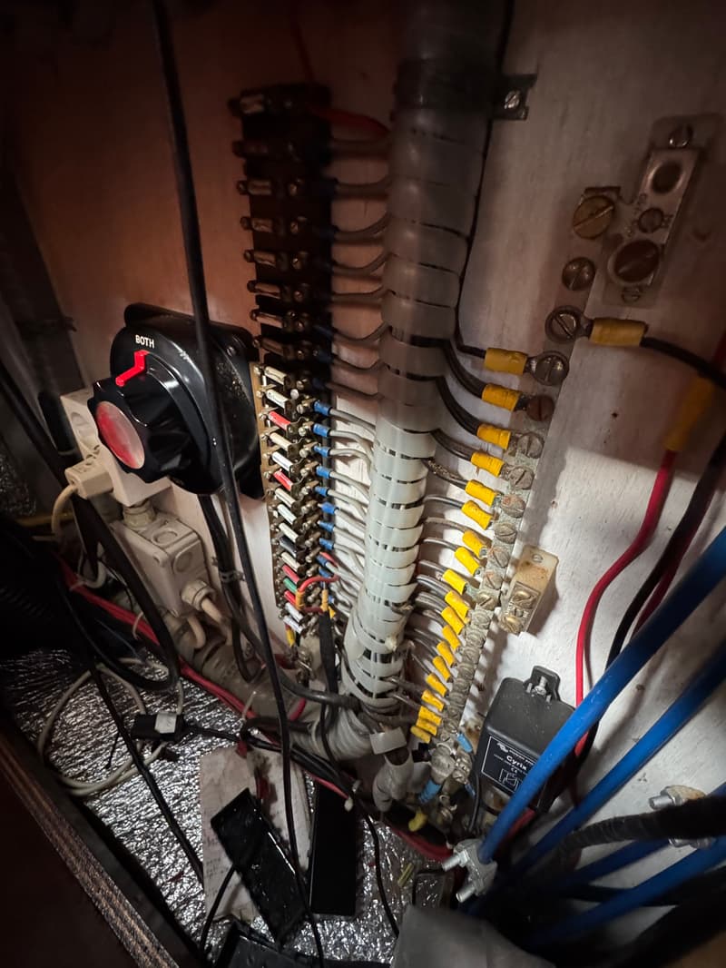Een detailfoto van een wirwar aan elektrische bedrading, zekeringen en een accuschakelaar met de tekst "BOTH".
