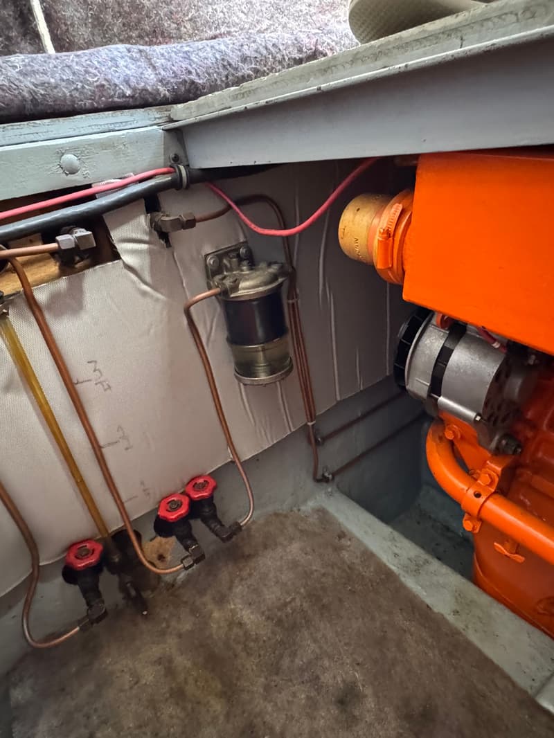 Een detailfoto van een oranje motorblok met een brandstoffilter, koperen leidingen en rode kranen in een boot.