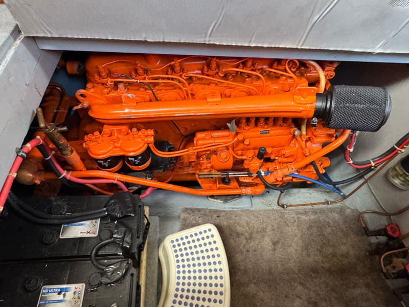 Een oranje scheepsmotor met twee zwarte accu's en een wit opstapje met blauwe stippen op een bruine vloer.