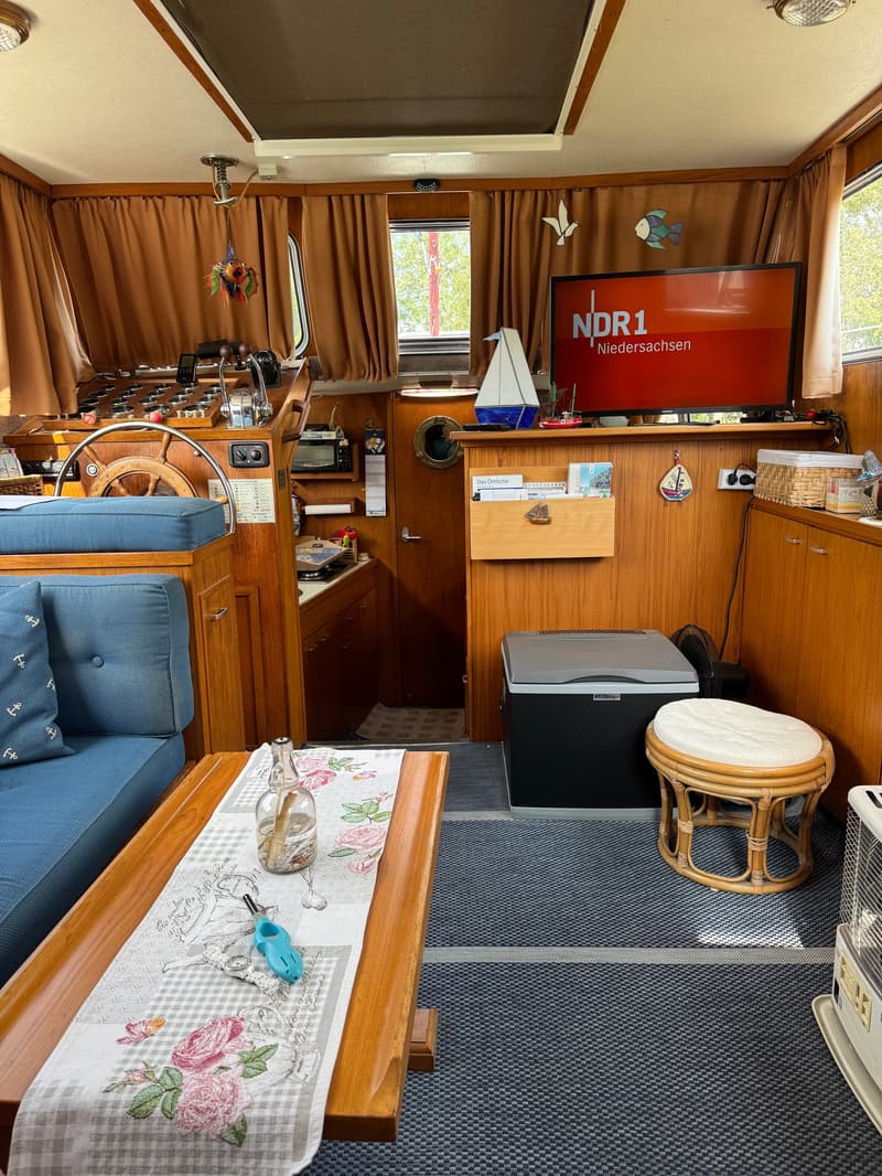 De foto toont het interieur van een boot met een stuurstand, zithoek, tv en een kleine keuken. — Neptunus 107 TWIN