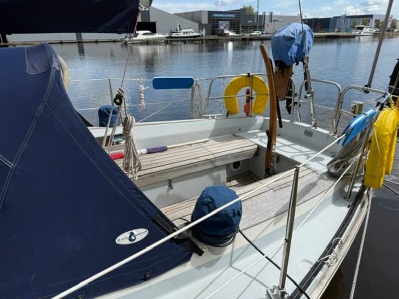 Een zeilboot ligt aangemeerd met een blauw afdekzeil over de giek en een houten roer. — Victoire 34 S-spant