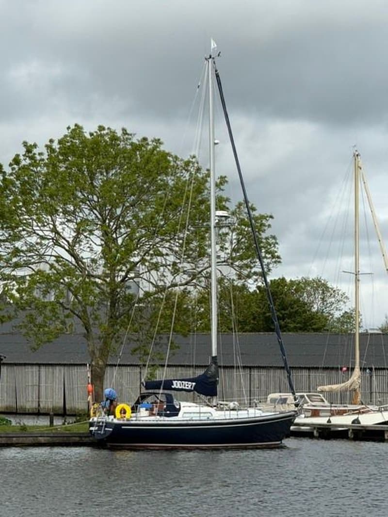 Een donkerblauwe zeilboot met de naam "JOODERT" op de giekhoes ligt afgemeerd aan een kade. — Victoire 34 S-spant