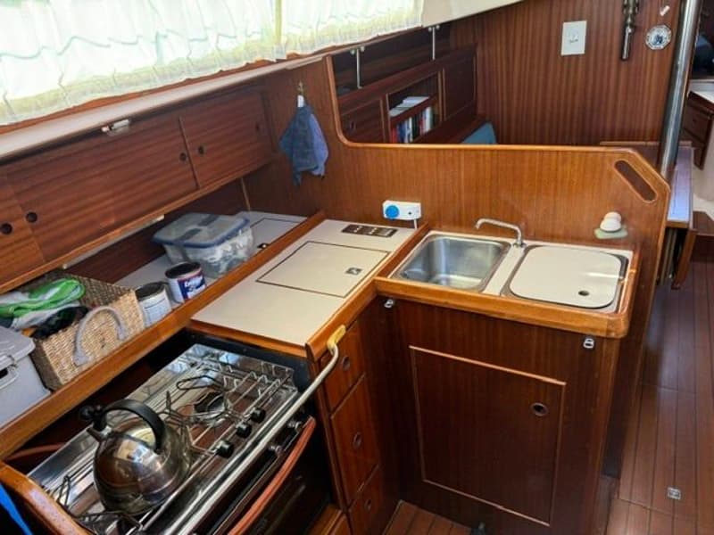De foto toont een houten interieur van een boot met een kombuis, inclusief een fornuis, gootsteen en opbergruimte.