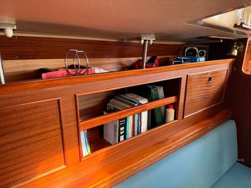 Een interieur van een boot met houten panelen, een blauwe bank en boeken in een open vak. — Victoire 34 S-spant