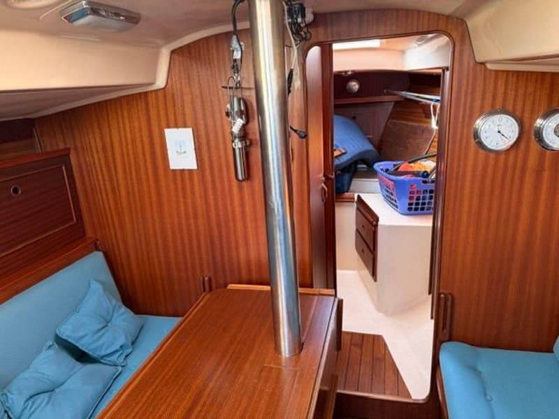 De foto toont het interieur van een boot met houten wanden, blauwe kussens en een tafel met een metalen paal.