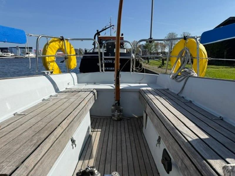 De foto toont de kuip van een zeilboot met houten banken en een houten vloer, met twee gele reddingsboeien aan de reling.