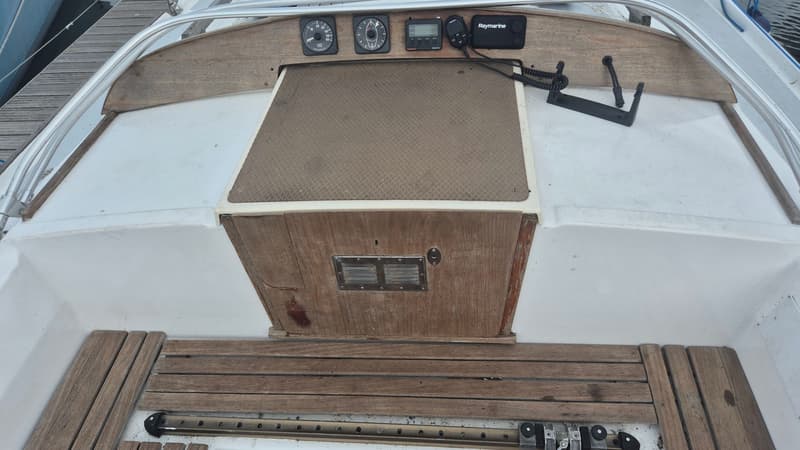 Een bovenaanzicht van een bootdek met houten panelen, instrumenten en een Raymarine marifoon.