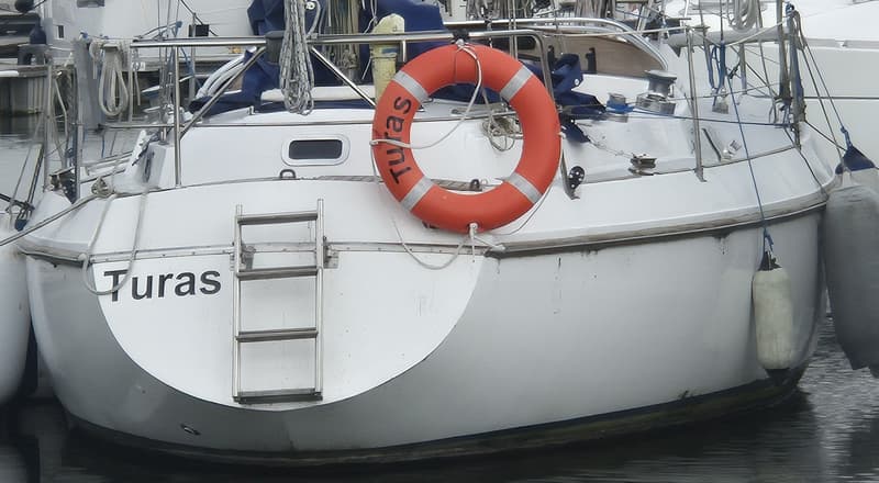 Een witte zeilboot met de naam "Turas" op de spiegel, een oranje reddingsboei en een zwemtrap. — Contest 36 Ketch