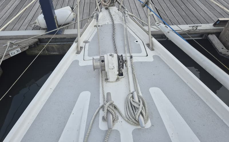 Een bovenaanzicht van de boeg van een witte zeilboot met grijze antislip, liggend aan een houten steiger. — Contest 36 Ketch