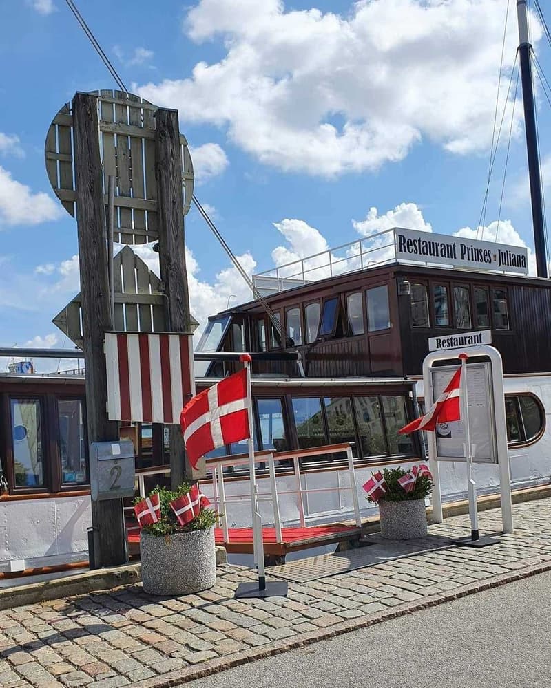 Een witte restaurantboot met bruine opbouw en ramen, genaamd "Restaurant Prinses Juliana", ligt aangemeerd.
