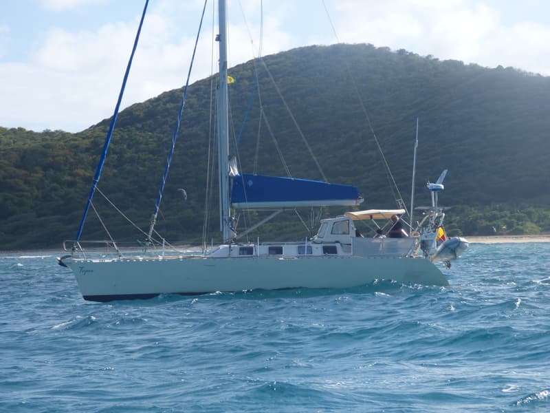 Een zeilboot met de naam "Tepee" op de boeg vaart op blauw water voor een groene, heuvelachtige kustlijn. — Navalu Faré 42