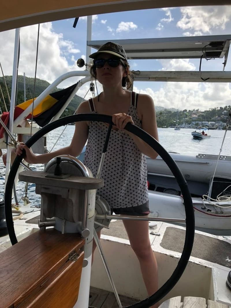 Een persoon met zonnebril en pet staat achter een zwart stuurwiel met een houten console op een boot. — Navalu Faré 42