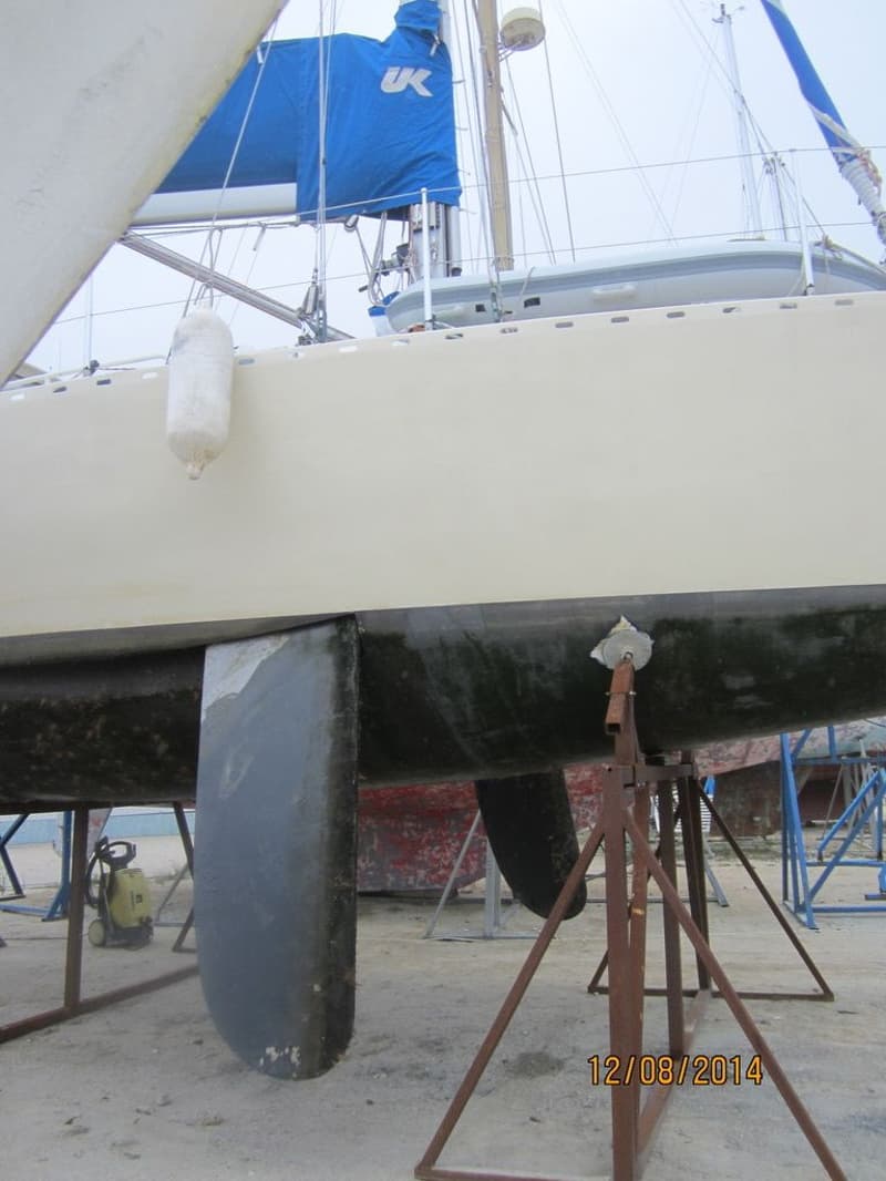Een zeilboot staat op de wal, ondersteund door stutten, met een blauwe zeilhoes met "UK" en een witte stootwil.