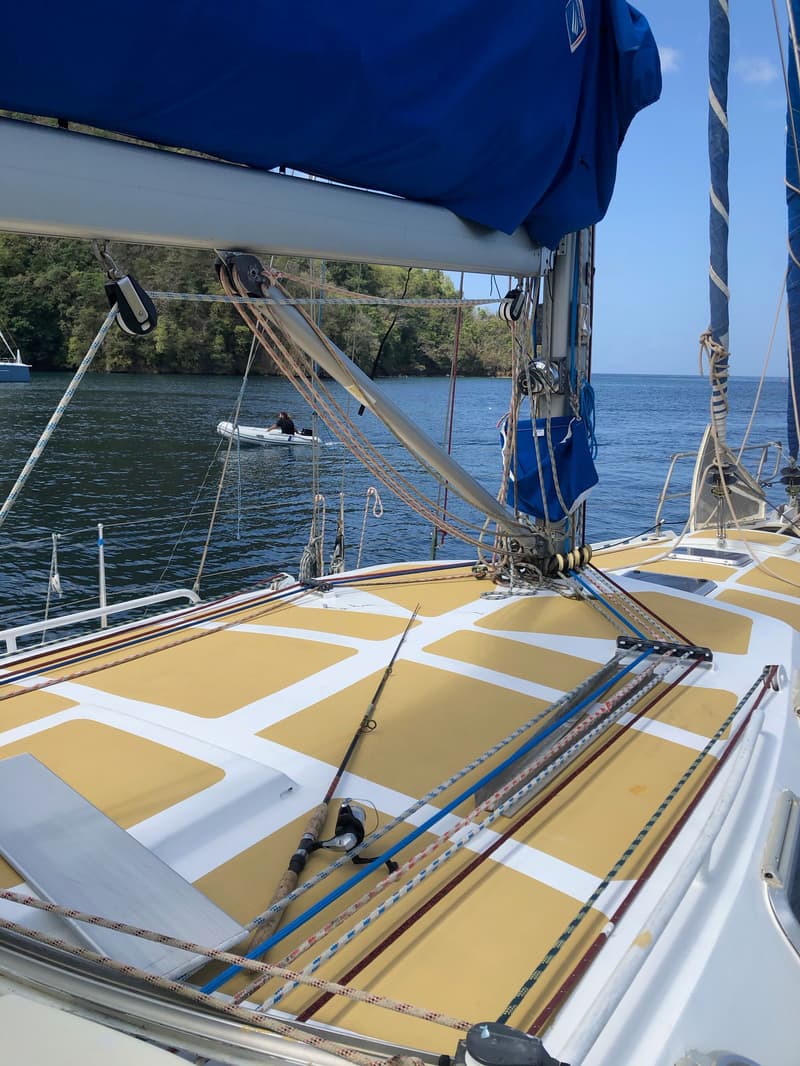 Het dek van een zeilboot met een geel-wit patroon, een blauwe zeilhuik, lijnen en een vishengel is zichtbaar.
