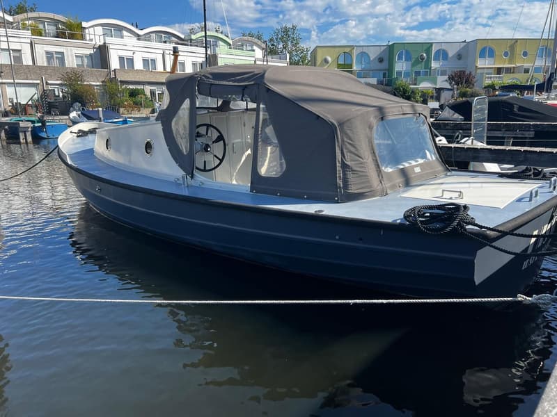 Een donkergrijze motorboot met een lichtgrijs dek en een donkergrijze buiskap ligt afgemeerd aan een steiger.