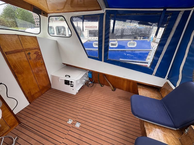 De foto toont het interieur van een boot met houten vloer, witte wanden, houten kasten en blauwe kussens.