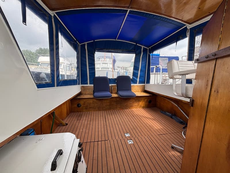 De foto toont het interieur van een boot met een blauwe kap, houten vloer en twee blauwe stoelen. — Ariadne kruiser 900 OK