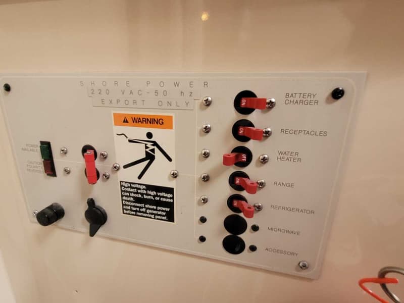 Een wit bedieningspaneel met rode schakelaars en zwarte knoppen, met waarschuwingsstickers en labels voor elektrische…