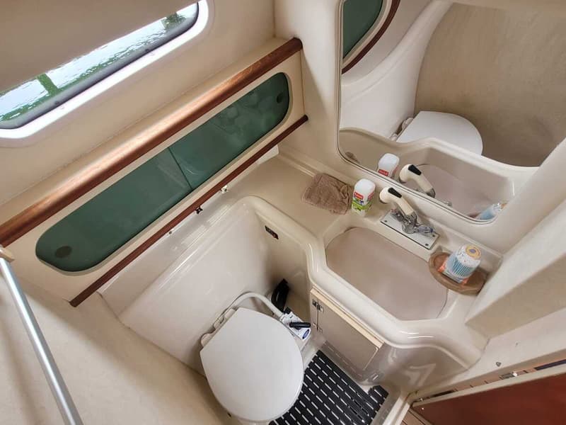 De foto toont een compacte badkamer in een boot met een toilet, wastafel met kraan, spiegel en een raam.
