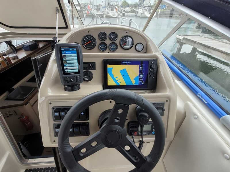 Een stuurstand met een stuurwiel, diverse meters, een Garmin GPS en een Simrad plotter met kaartweergave.