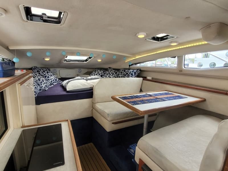 De foto toont een kajuit met een bed, een zithoek met tafel en een kookplaat. — Bayliner 2855 Ciera Sunbridge