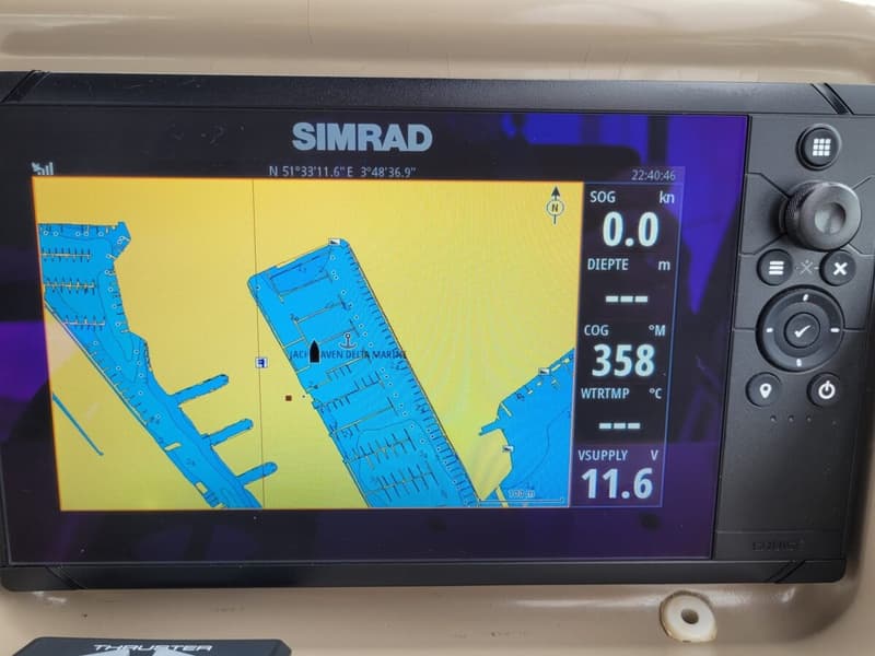 Een Simrad navigatiescherm toont een kaart van een jachthaven met coördinaten, snelheid, diepte, koers en accuspanning.
