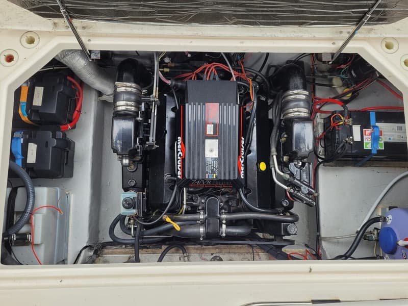 De foto toont een motorruimte met een zwarte Mercruiser 7.4L V8 motor, omringd door accu's en diverse slangen en kabels.