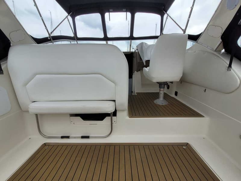 De foto toont het interieur van een boot met witte zitplaatsen, een stuurstand en een houten vloer.