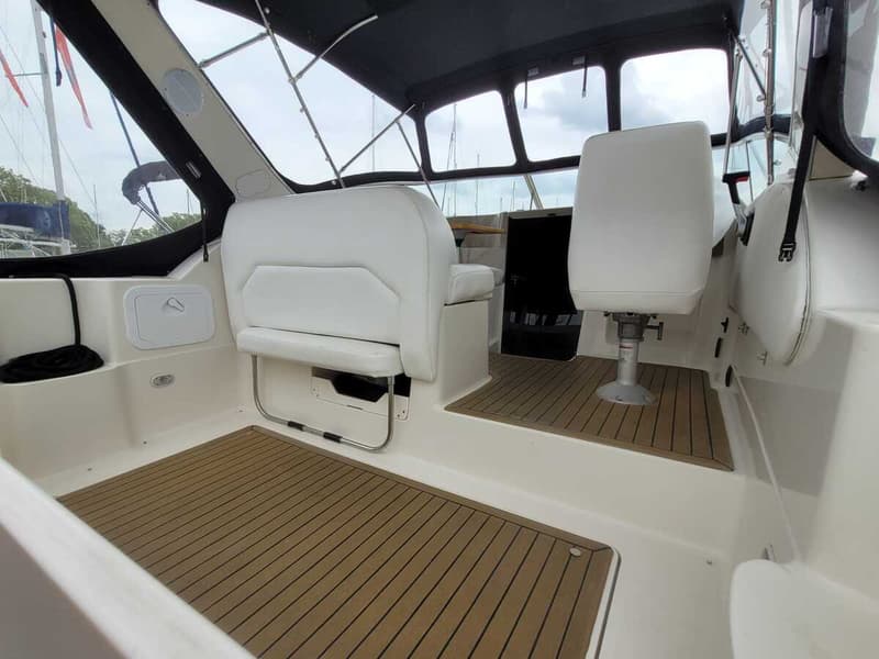 De foto toont het interieur van een boot met witte stoelen, een bruine vloer en een zwart afdak.
