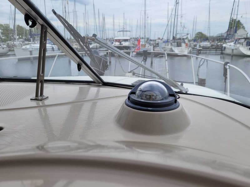 Een kompas is gemonteerd op het dashboard van een boot, met een jachthaven op de achtergrond. — Bayliner 2855 Ciera Sunbridge