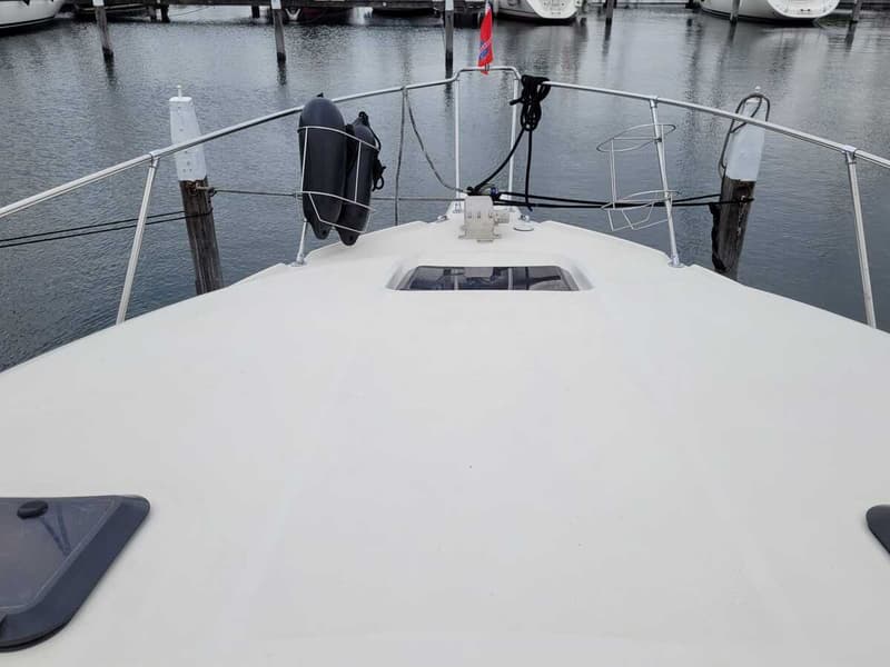 De foto toont de boeg van een witte boot met een reling, stootwillen en een luik, liggend in een haven.