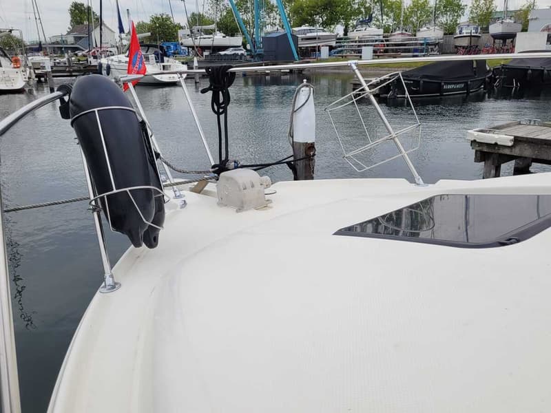 Een witte boot ligt aangemeerd in een haven, met een zwart stootkussen en een metalen rek op het dek.