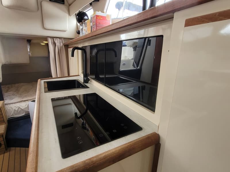 Een bootkeuken met een zwarte spoelbak, een zwarte kraan en een zwarte inductiekookplaat.