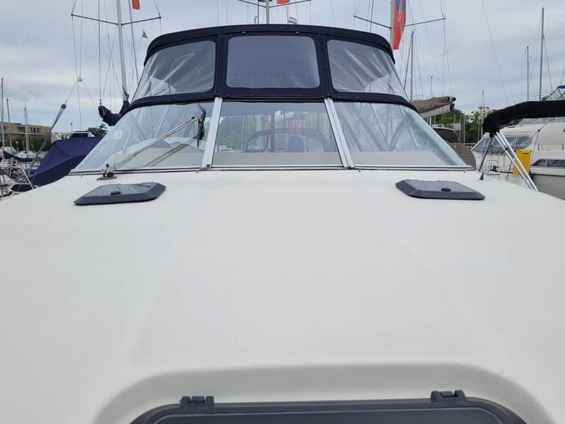 De foto toont het voordek van een boot met twee luiken, een voorruit en een donkerblauwe cabriokap.