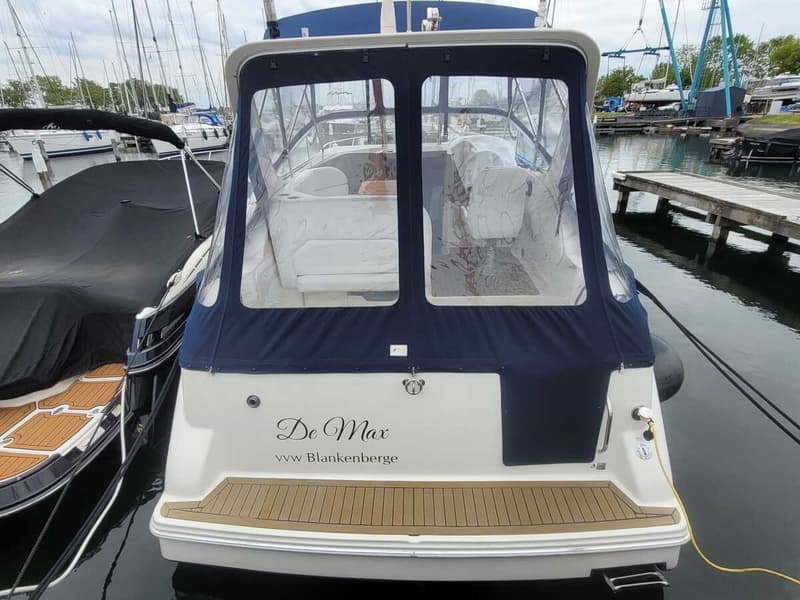 De achterkant van een witte boot met een blauwe kap en de naam "De Max vvw Blankenberge" erop, ligt in een haven.