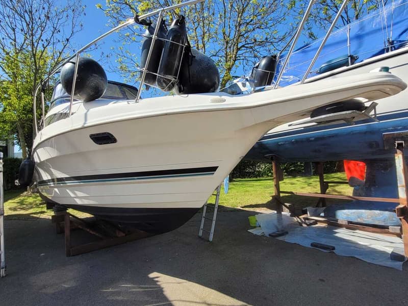 Een witte boot staat op houten bokken op een geasfalteerde ondergrond, met een blauwe boot ernaast.