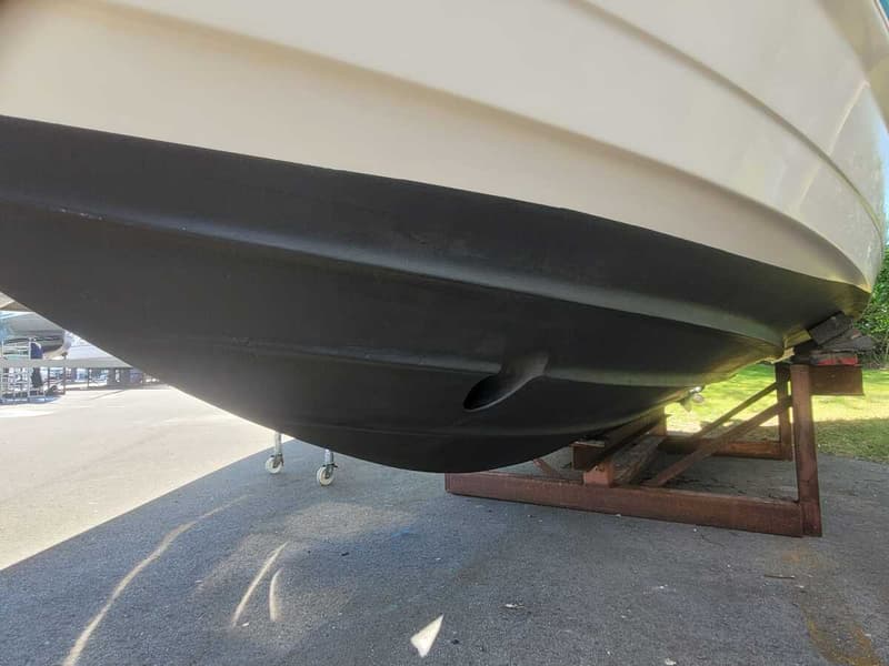 De onderkant van een boot, deels zwart en deels wit, staat op een bruine houten bok op een grijze ondergrond.