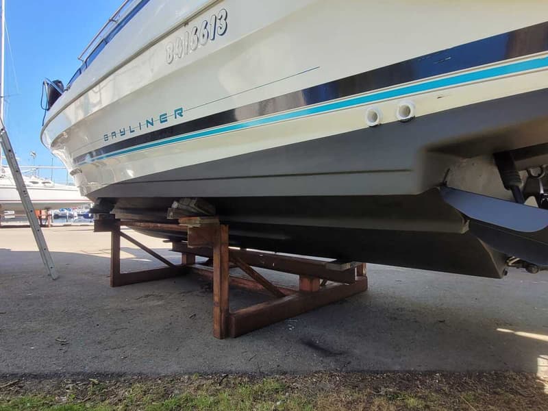 Een witte boot met de naam "BAYLINER" en het nummer "8916613" op de zijkant staat op een houten bok op het droge.