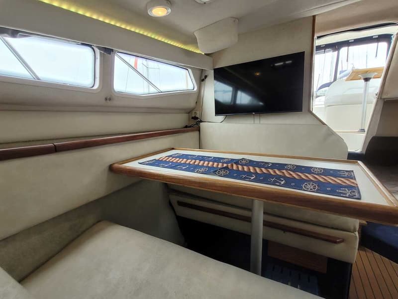 De foto toont een interieur van een boot met een tafel, banken, ramen en een televisie. — Bayliner 2855 Ciera Sunbridge