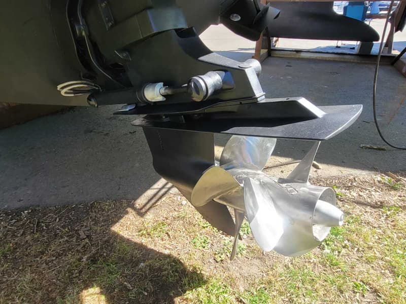 Een detailfoto van een bootmotor met een zilverkleurige driebladige schroef en een zwarte staartstuk.
