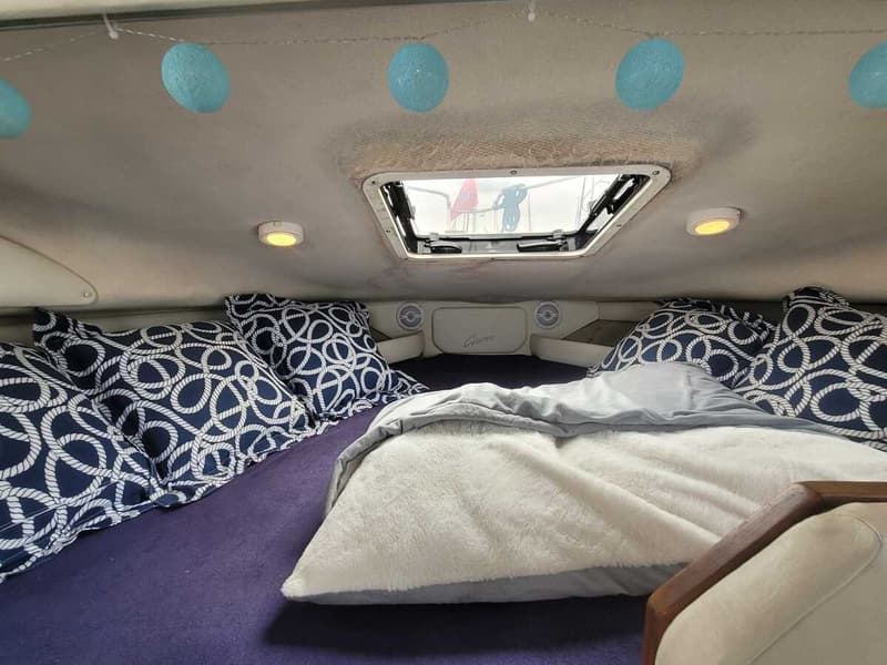 Een kajuit met een bed, kussens met een touwpatroon, een deken, een dakraam en blauwe lichtslingers.