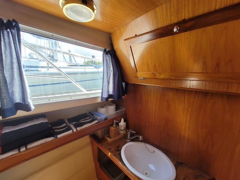 Een houten interieur van een boot met een wastafel, een raam met gordijnen en een opbergvak. — Agder 840 OK