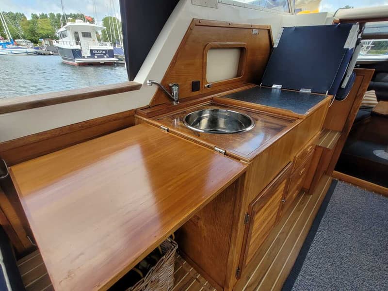 Een houten kombuis met een ronde spoelbak, kraan, een opklapbaar werkblad en een kookplaat met deksel.