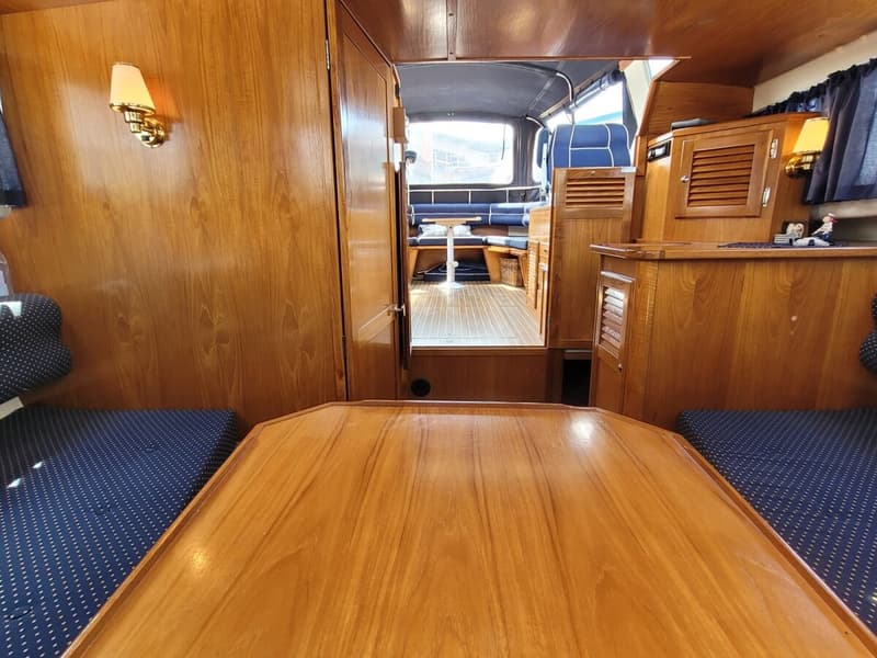 Een interieur van een boot met houten wanden, een houten tafel en blauwe kussens met witte stippen. — Agder 840 OK