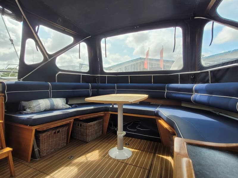 Een interieur van een boot met een U-vormige zitbank met blauwe kussens, een houten tafel en een houten vloer. — Agder 840 OK