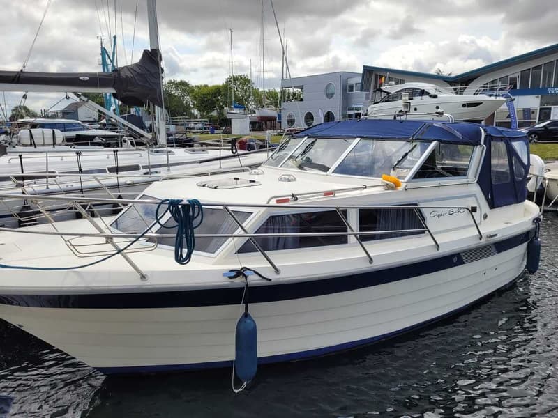 Een witte motorboot met blauwe accenten en een blauwe kap ligt in het water, met de — Agder 840 OK