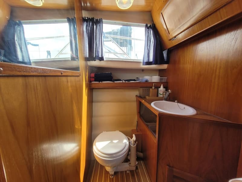 Een houten interieur met een toilet, een wastafel met kraan en een spiegel, verlicht door daglicht en lampen.