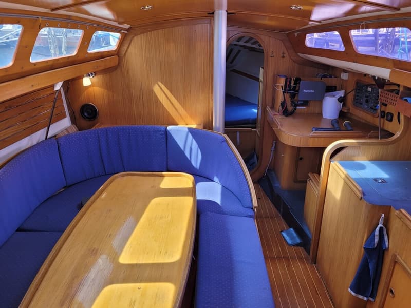 De foto toont het interieur van een boot met houten wanden, een blauwe U-vormige bank en een houten tafel. — Feeling 346