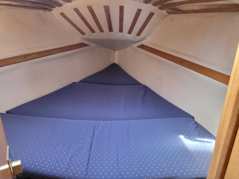 De foto toont een kajuit met een blauw matras met oranje stippen en houten latten aan het plafond en de zijkanten.